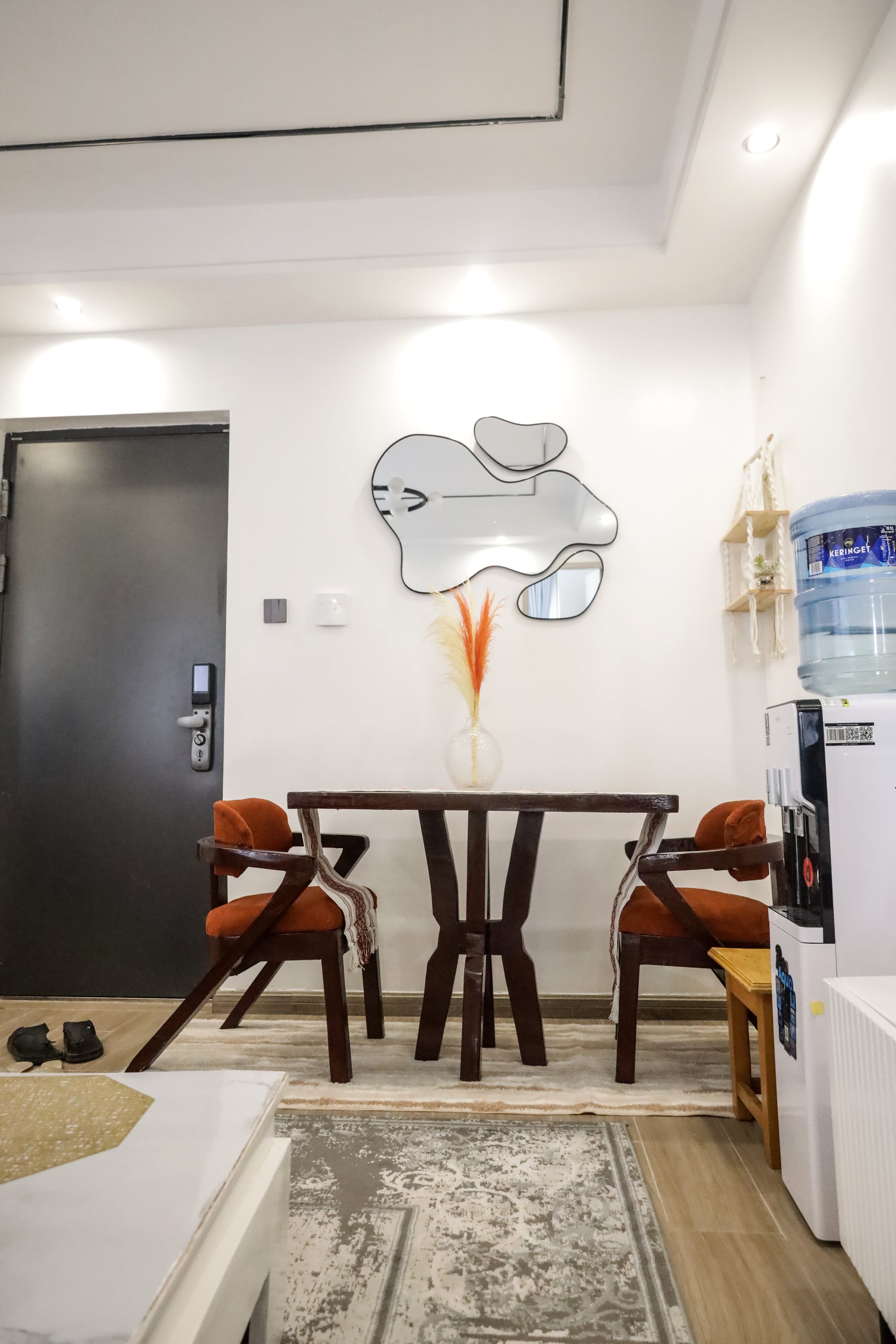 Entry door beside a round hardwood dining table with burnt-orange chairs and a sculptural wall mirror