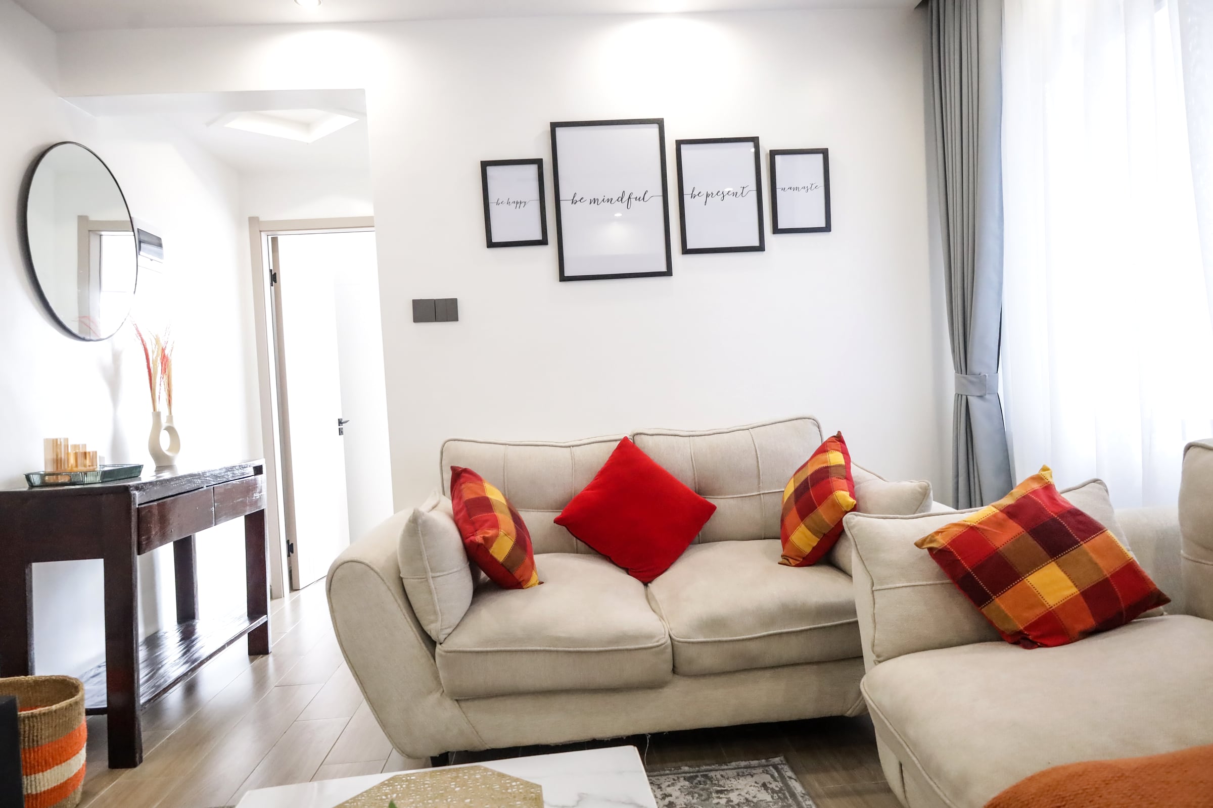 Cream sofa dressed with red and plaid cushions beneath a row of framed prints