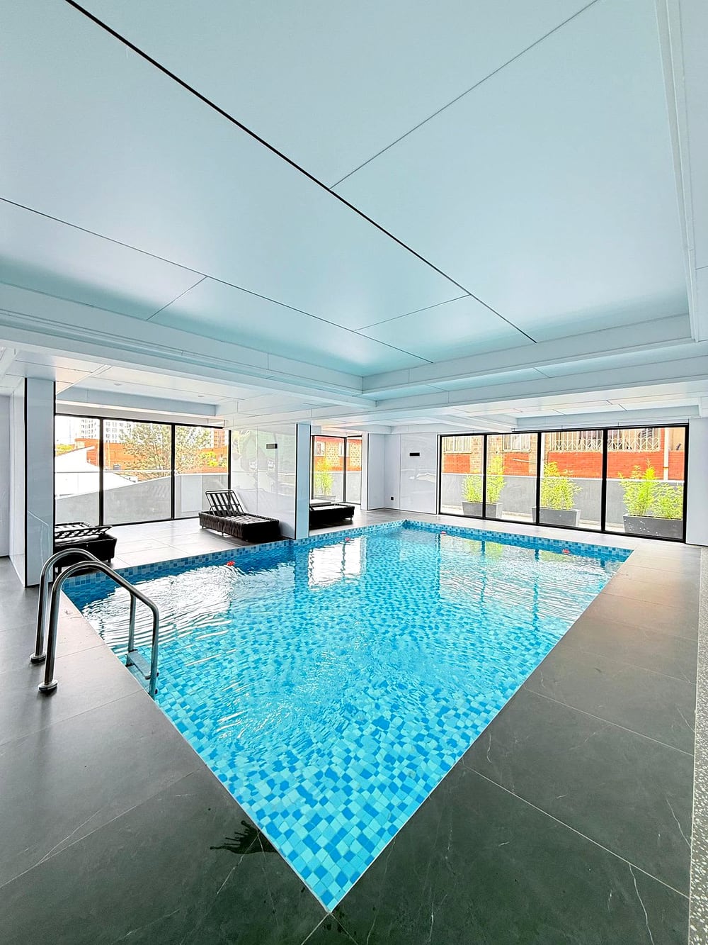 Indoor heated pool with blue mosaic tiling, loungers and a wall of windows